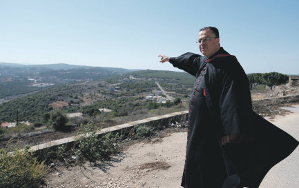 L’archevêque maronite de Tyr, Monseigneur Abdallah, montre la frontière avec Israël, située au sommet de la colline visible au loin. / ©Gaby Leygues