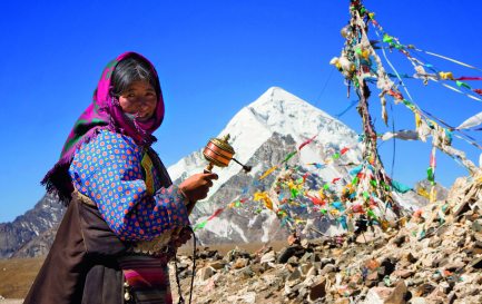 Moulin à prières dans la main, une pèlerine bouddhiste s’est arrêtée devant les petits drapeaux sur lesquels les Tibétains écrivent des invocations que le vent emporte vers les divinités. / © Christopher Tozer/Alamy Stock Photo